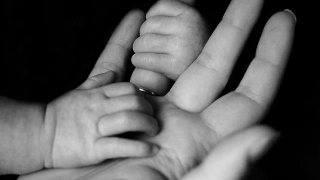 A black and white photo of a baby holding a parent's hand. 