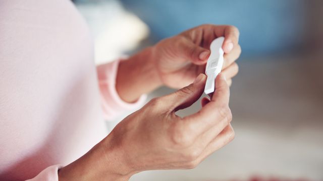 A person wearing a pink jumper holds a pregnancy test. 