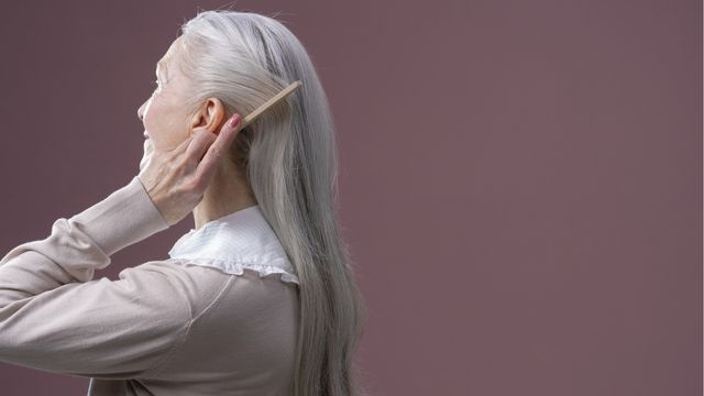 An older woman combing her long gray hair. 