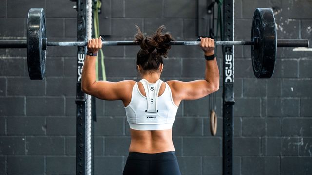 A woman lifts a bar with weights on the end above her head. 