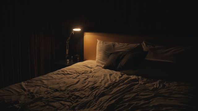 A bed lit by a bedside lamp. 
