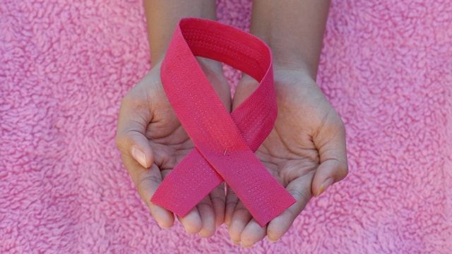 Person holding a folded pink ribbon representing breast cancer support against the background of a pink fury blanket. 