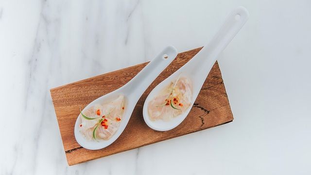 Two ceramic presentation spoons with ceviche on presented on a wooden board. 
