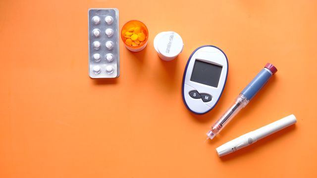 A collection of pills and blood sugar testing equipment on an orange background. 